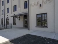 an empty sidewalk by a building with windows and stairs to the door and floor, and a railing on the ground, near it is a parking lot that leads to a fire hydrant