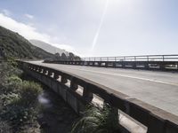 the sun shines brightly over an empty highway that is bordered with scrub vegetation, and the ocean