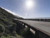 the sun shines brightly over an empty highway that is bordered with scrub vegetation, and the ocean