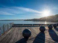 five steel balls are sitting on the pier overlooking water with sun shining over the ocean and city in the background