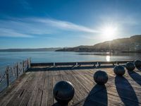 five steel balls are sitting on the pier overlooking water with sun shining over the ocean and city in the background