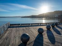 five steel balls are sitting on the pier overlooking water with sun shining over the ocean and city in the background