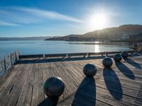 five steel balls are sitting on the pier overlooking water with sun shining over the ocean and city in the background