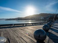 five steel balls are sitting on the pier overlooking water with sun shining over the ocean and city in the background