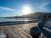 five steel balls are sitting on the pier overlooking water with sun shining over the ocean and city in the background