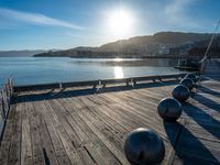 five steel balls are sitting on the pier overlooking water with sun shining over the ocean and city in the background