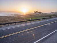 a car traveling down an empty highway at sunset by the ocean with a beautiful sun in the sky