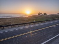 a car traveling down an empty highway at sunset by the ocean with a beautiful sun in the sky