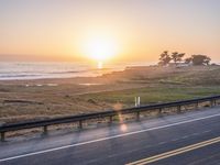 a car traveling down an empty highway at sunset by the ocean with a beautiful sun in the sky