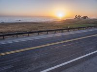 a car traveling down an empty highway at sunset by the ocean with a beautiful sun in the sky