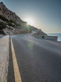 a man is riding on the road on the mountain top next to the ocean and cliff