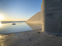 a sunset with sun rising over the water and a large concrete structure on it's side