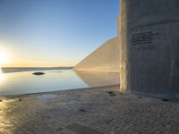 a sunset with sun rising over the water and a large concrete structure on it's side