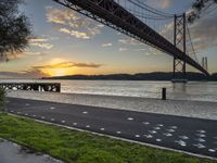 a man in a red jacket riding a bike past a bridge at sunset by the water