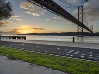 a man in a red jacket riding a bike past a bridge at sunset by the water