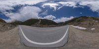 a road curves in a very cloudy sky near mountains with snow on it and a blue sky