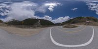 a road curves in a very cloudy sky near mountains with snow on it and a blue sky