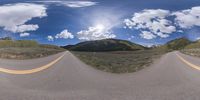 a road curves in a very cloudy sky near mountains with snow on it and a blue sky