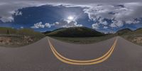 a road curves in a very cloudy sky near mountains with snow on it and a blue sky