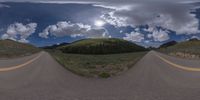 a road curves in a very cloudy sky near mountains with snow on it and a blue sky