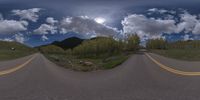 a road curves in a very cloudy sky near mountains with snow on it and a blue sky