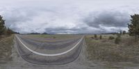 a road curves in a very cloudy sky near mountains with snow on it and a blue sky