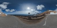 a road curves in a very cloudy sky near mountains with snow on it and a blue sky