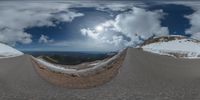 a road curves in a very cloudy sky near mountains with snow on it and a blue sky