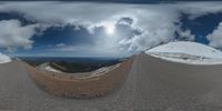 a road curves in a very cloudy sky near mountains with snow on it and a blue sky