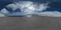 a road curves in a very cloudy sky near mountains with snow on it and a blue sky