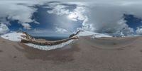 a road curves in a very cloudy sky near mountains with snow on it and a blue sky