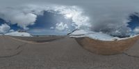 a road curves in a very cloudy sky near mountains with snow on it and a blue sky