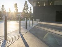 large cement sidewalk and metal poles in front of a building with a bright light coming through the window