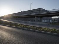 the sun shines brightly over a roadway bridge on an otherwise empty road while vehicles are passing below