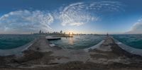 an image of sunset at the ocean taken by a fish eye lens with buildings in the background