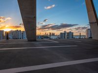 the sun setting on a rooftop with a view of buildings in the distance and a few parked cars