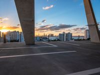 the sun setting on a rooftop with a view of buildings in the distance and a few parked cars