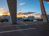 the sun setting on a rooftop with a view of buildings in the distance and a few parked cars