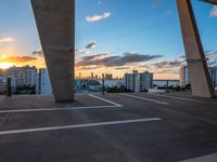 the sun setting on a rooftop with a view of buildings in the distance and a few parked cars