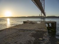 a bridge that is over the water with some boats underneath it at sunrise time in the background