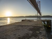 a bridge that is over the water with some boats underneath it at sunrise time in the background