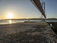 a bridge that is over the water with some boats underneath it at sunrise time in the background