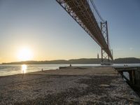 a bridge that is over the water with some boats underneath it at sunrise time in the background