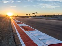 a photo of a dirt race track with sun setting in the distance of the track