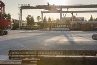 construction equipment and equipment sit in a warehouse in the sunlight in the background is a large crane