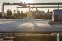 construction equipment and equipment sit in a warehouse in the sunlight in the background is a large crane