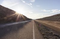 the sun shines brightly on a dirt road by the mountains near an empty roadway