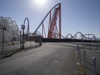 a roller coaster and an airplane going by at a theme park setting with a bright sun