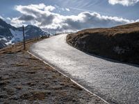 a long paved road with a snowy mountain in the distance and a trail going behind it