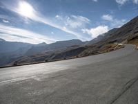 a motorcycle driving along a winding road through a valley to mountains and peaks in the background